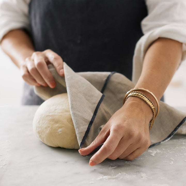 Model covering the dough with the Cara Edged Napkin in Slate. The model is wearing a dark apron.