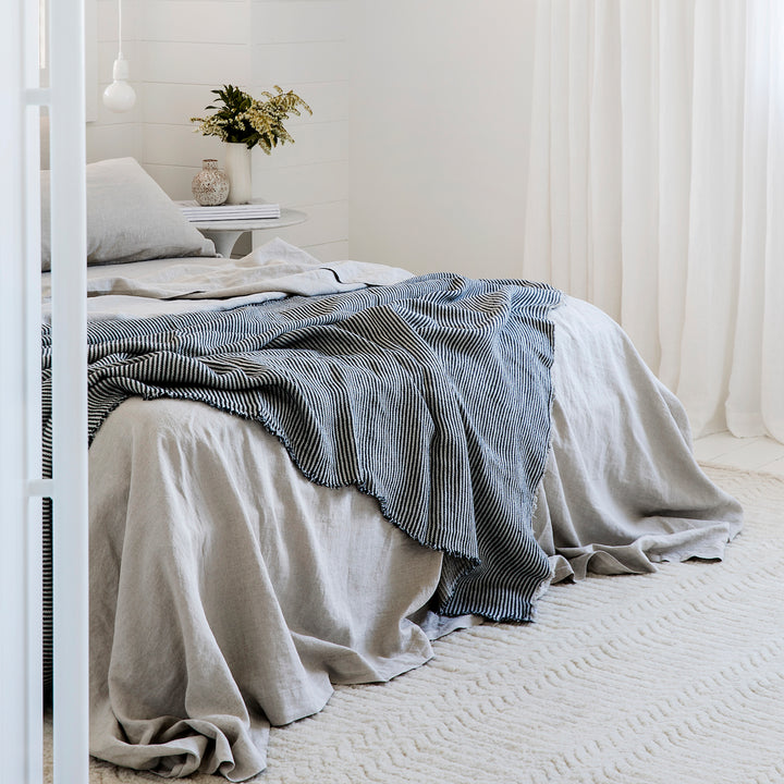 A bed dressed in a Linen Sheet Set in Smoke Grey, paired with a Mira Ellis Stripe Bedcover. Available in Single, Double, King, Super King.
