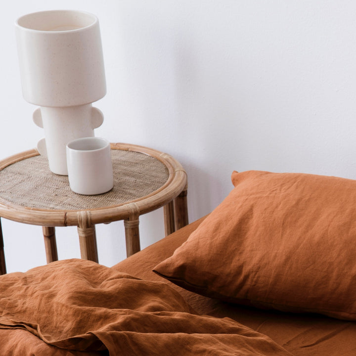 A close up of a bed dressed in Cedar bed linen, styled a ceramic vase and cup sitting on top of a bamboo bedside table. Available in Double, King, Super King.