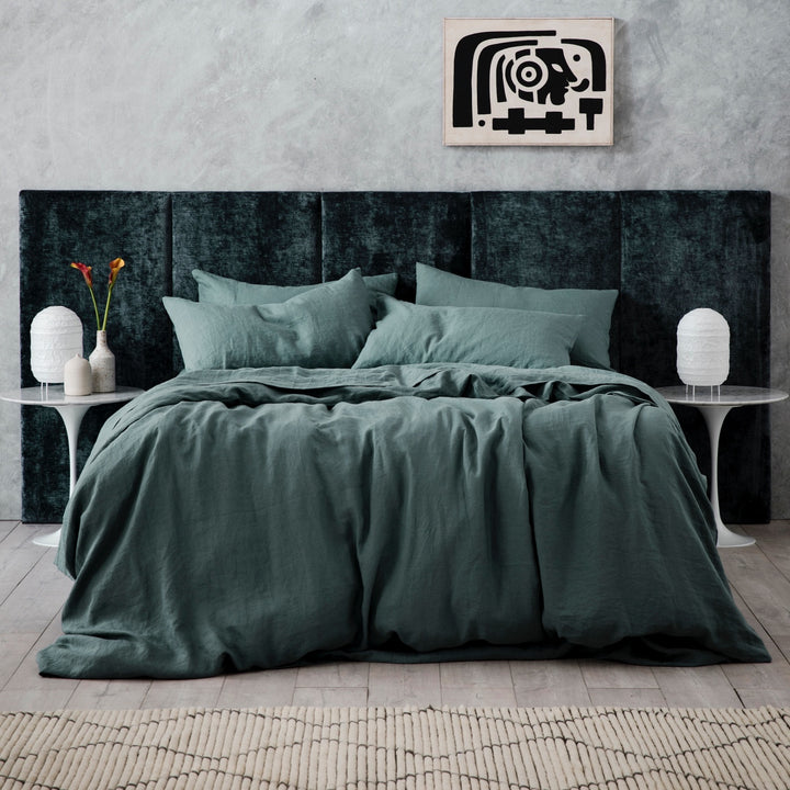  A bed dressed in Bluestone bed linen, styled with a velvet headboard, two white bedside tables, ceramic vases and a white lantern lamp. Available in Single, Double, King, Super King.