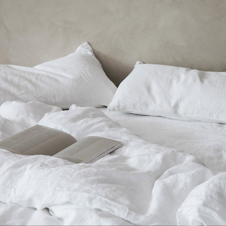 A bed dressed with linen bedding in White. On top of the bed is an open book. Available in Double, King, Super King.
