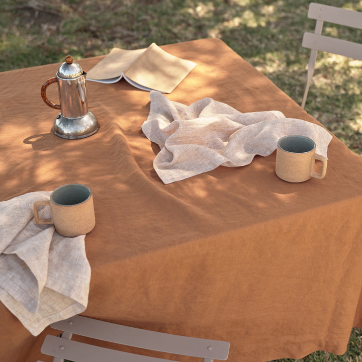 A close up of a casual outdoor table setting featuring a Linen Tablecloth in Cedar, paired with Linen Napkins in Cinnamon. Available in Small 150cm x 240cm & Medium 180cm x 300cm.
