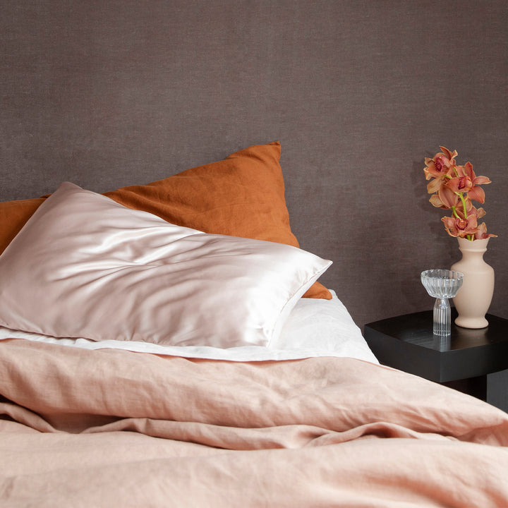 A bed dressed in Fawn, Blush and Cedar bed linen, styled with a black side table, and a pale pink vase with orchids. Available in Double, King, Super King.