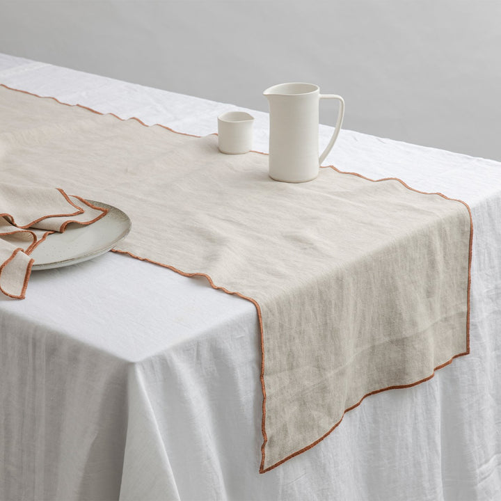 Cara Edged Table Runner in Cedar on a Linen Tablecloth in White