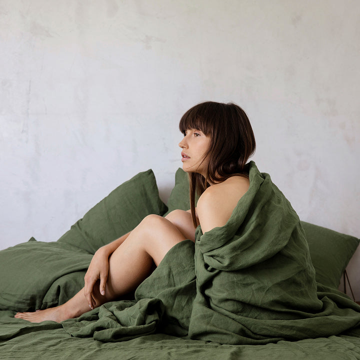 A woman sitting on a bed dressed in Forest bed linen. Available in Single, Double, King & Super King.