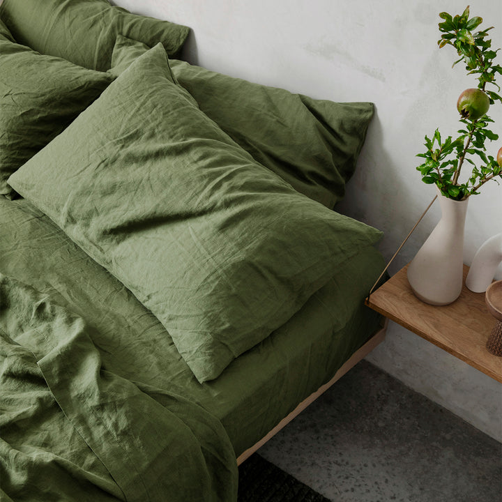 A close up of a bed dressed in Forest bed linen, styled with a floating wooden bedside table and a vase with greenery. Available in Double, King & Super King.