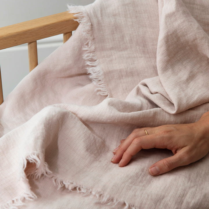  A close up of a hand placed on a Freya Linen Throw in Blush