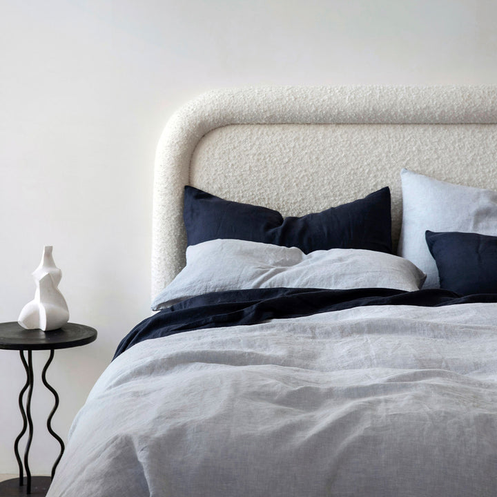 A cream bed dressed in Navy and Sky bed linen, styled with a modern black bedside table and small white ornament. Available in Double, King, Super King.