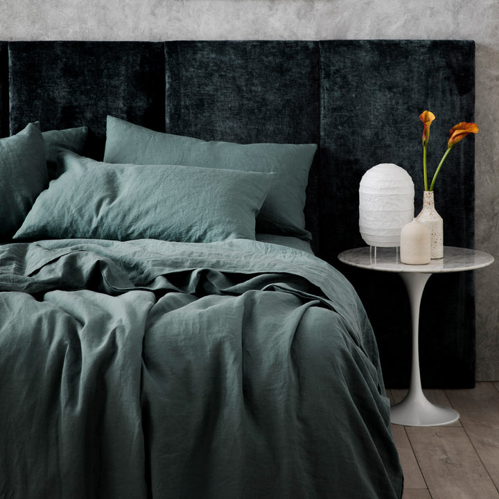  A bed dressed in Bluestone bed linen, styled with a velvet headboard, white bedside table, two ceramic vases and a white lantern lamp. Available in Single, Double, King, Super King.