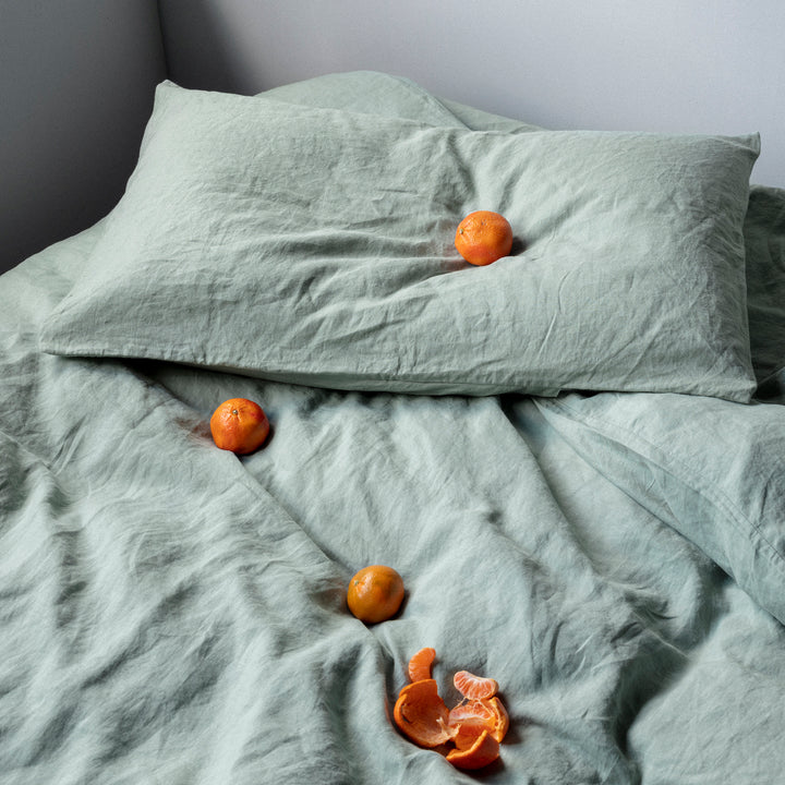 A bed dressed in Sage bed linen styled with mandarins. Available in Single, Double, King, Super King.