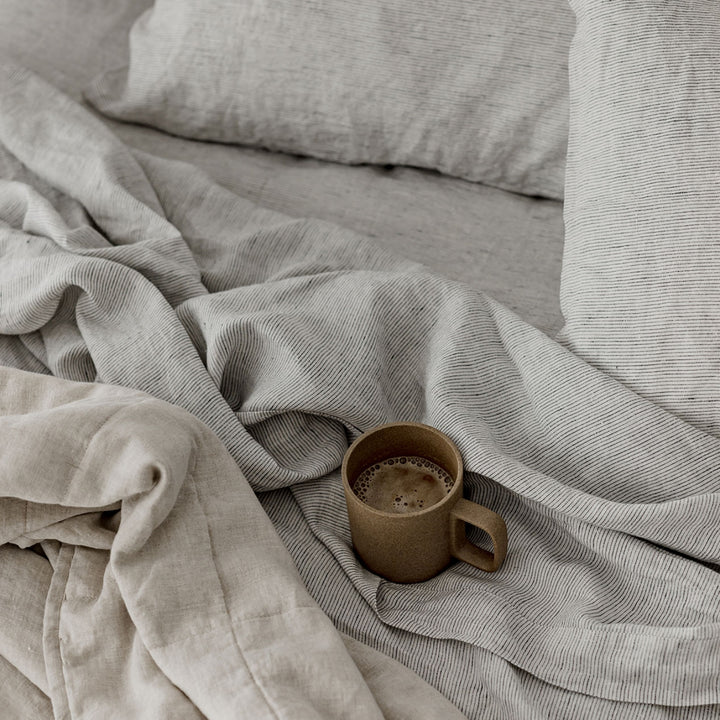 A coffee mug resting on a bed dressed in Pinstripe and Natural linen