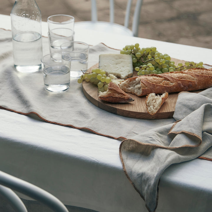 A close up of a cheese platter on an outdoor dining table styled with a Cara Edged Table runner in Cedar and a Cara Edged Napkin in Natural