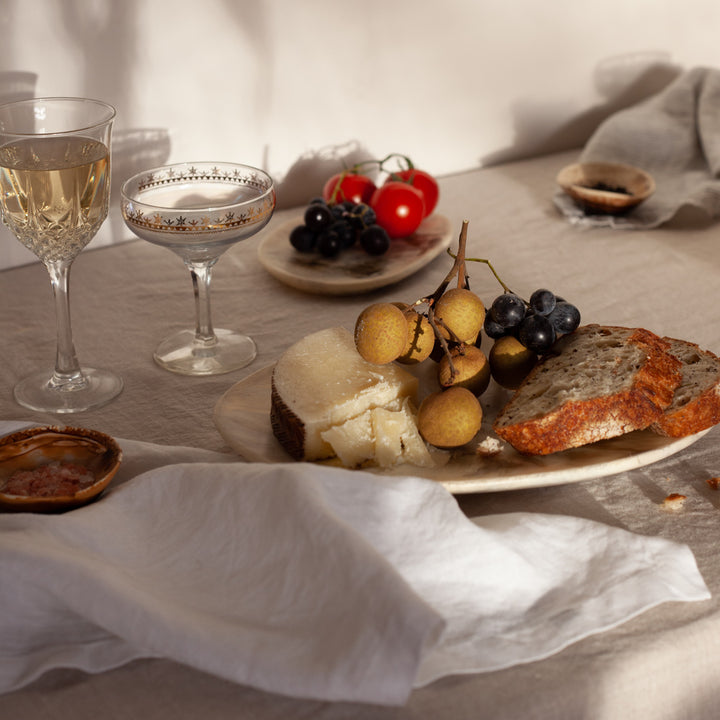 A close up table setting featuring a White Napkin on a Natural Tablecloth with grazing food.