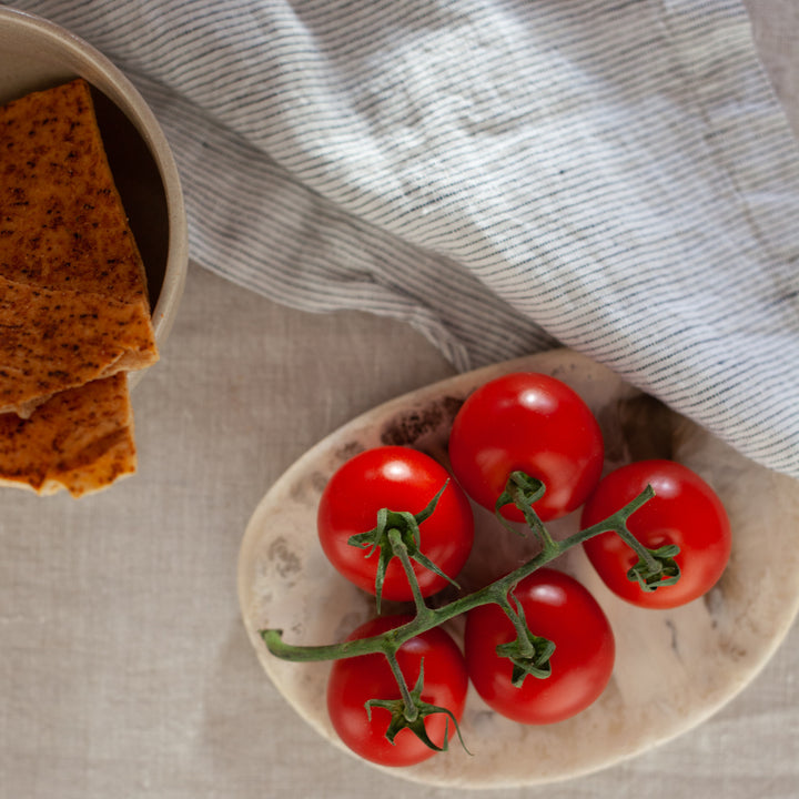  A close up of a Linen Table Napkin in Pinstripe, placed next to a bowl of tomatoes and a bowel of crackers