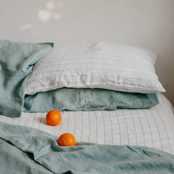 A bed dressed in Sage and Pencil Stripe bedlinen, with oranges scattered on the Duvet Cover. Available in Standard & King.