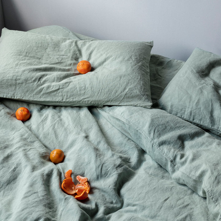 A bed dressed in Sage bed linen, styled with mandarins. Available in Single, Double, King, Super King.