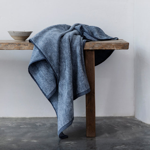  A denim bath towel draped on a bench. Available as Bath Towel Bundle & Bath Sheet Bundle.