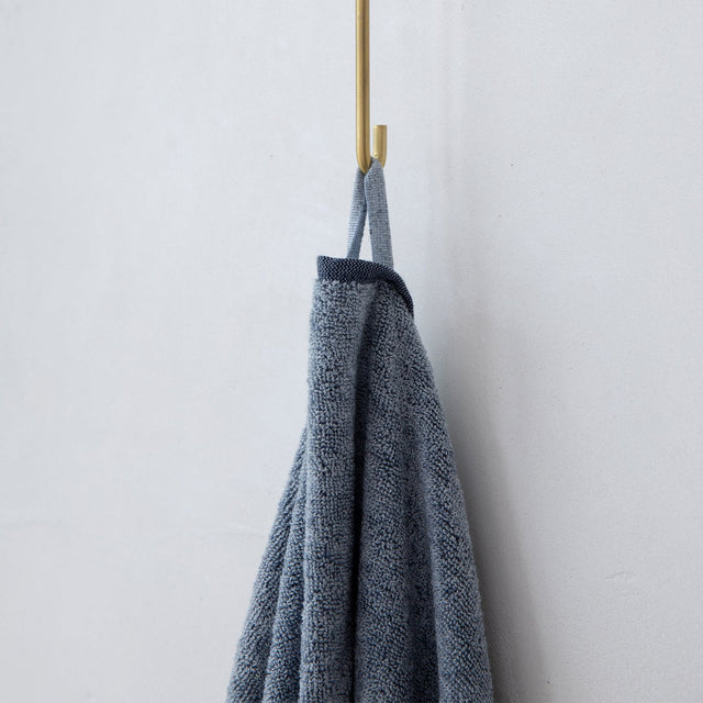  A close up photo of a Denim bath towel hanging on hook. Available as Bath Towel 70cm x 140cm & Bath Sheet 90cm x 175cm.
